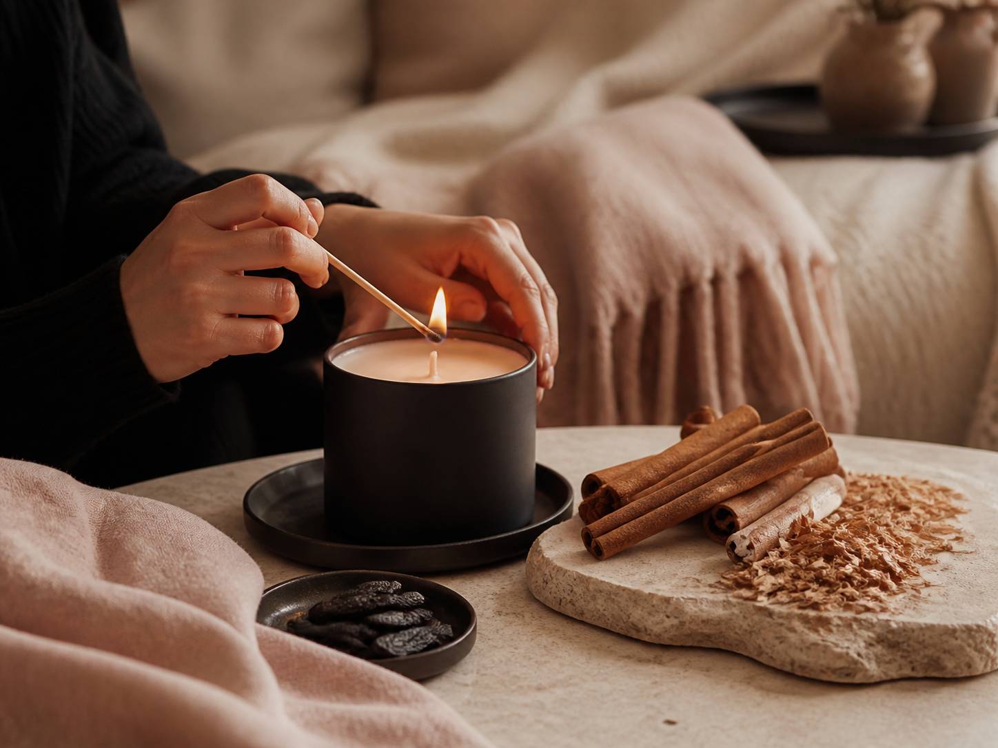Mains allumant une bougie entourée de cannelle et de cèdre