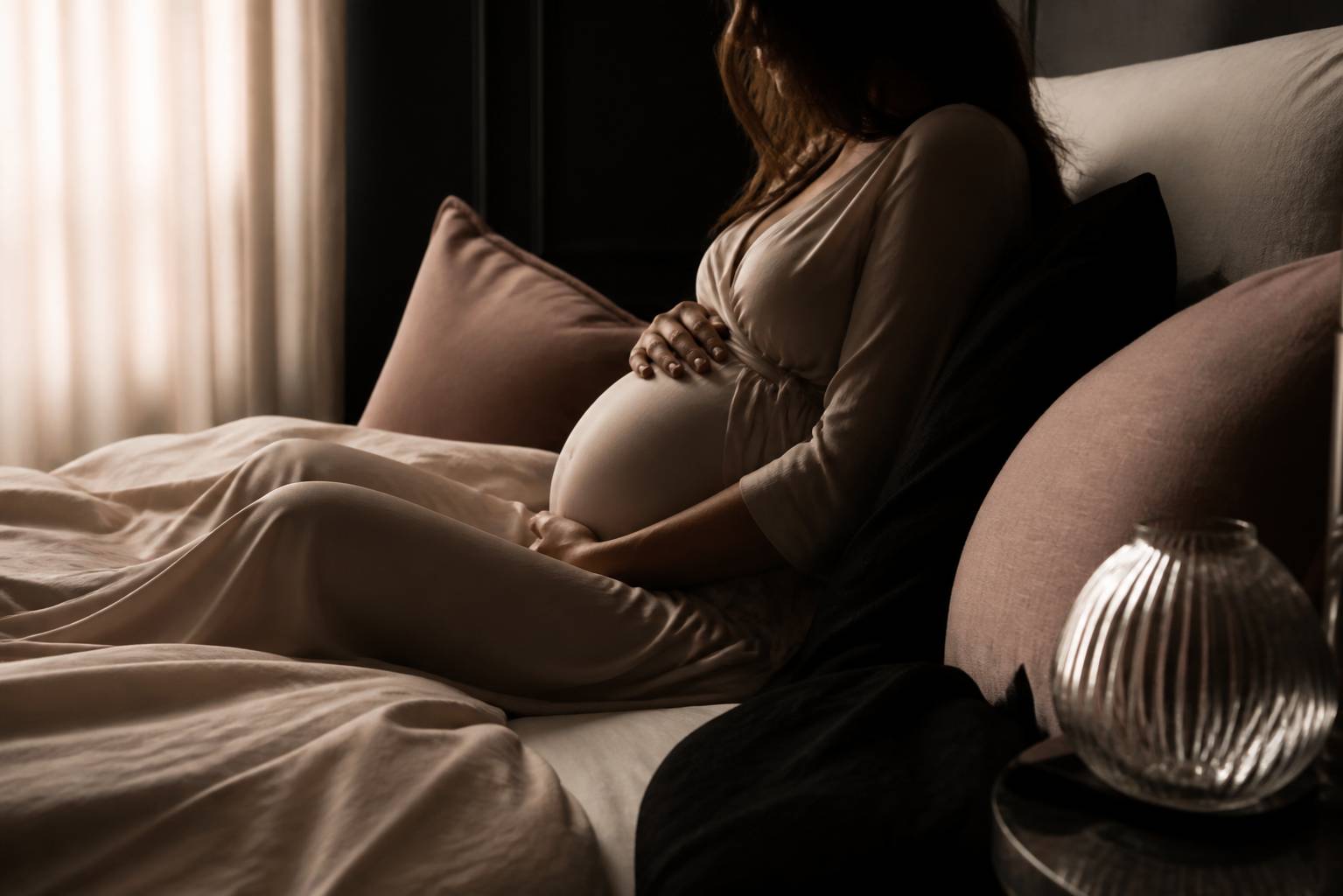 Silhouette d'une femme enceinte assise sur un lit, appuyée sur des coussins